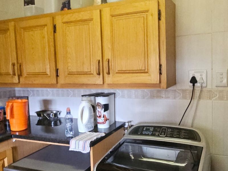 A functional laundry area featuring built-in wooden cabinetry, granite countertops, and tiled splashbacks, providing practical storage and workspace for household utility tasks.