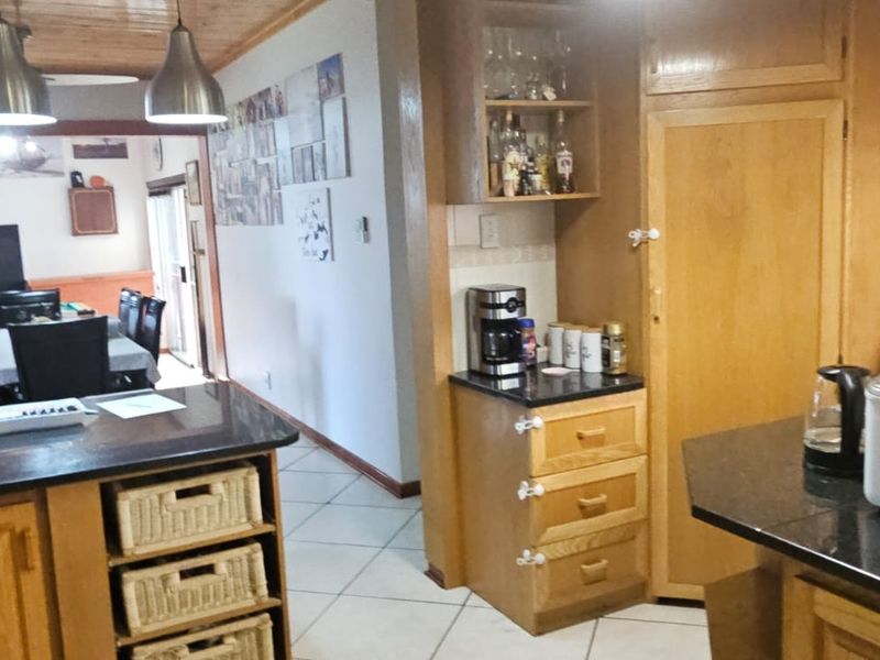 Open plan kitchen and dining area featuring wooden cabinetry, granite countertops, tiled flooring, and a timber ceiling with pendant lighting.
