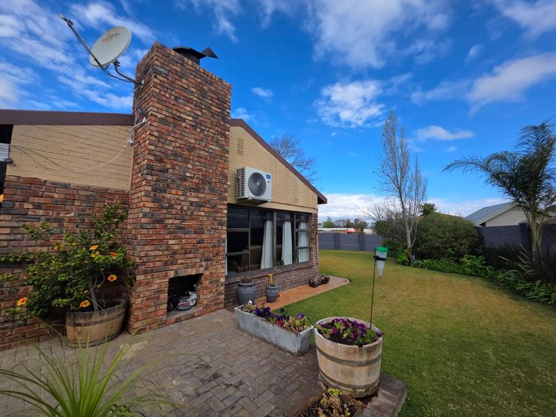 Rear view of the property featuring a brick chimney with an integrated outdoor fireplace, paved patio area, and a well-maintained garden.