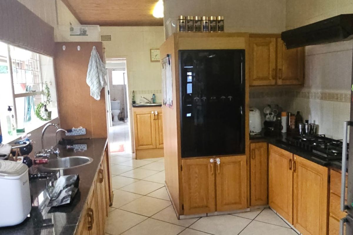 A functional kitchen featuring wooden cabinetry, granite countertops, a gas hob with extractor fan, and tiled flooring, with a view into the adjacent utility area.