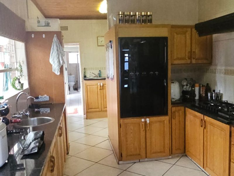 A functional kitchen featuring wooden cabinetry, granite countertops, a gas hob with extractor fan, and tiled flooring, with a view into the adjacent utility area.