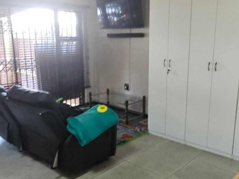 A living room featuring tiled flooring, built-in storage cupboards, and a security gate over the window.