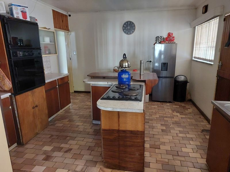 A dated kitchen featuring original wood-finish cabinetry, a built-in oven, electric hob, and tiled flooring, offering significant potential for a modern renovation.