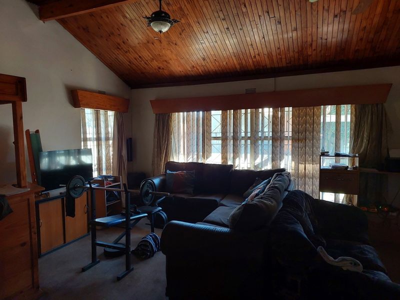 Spacious living room featuring a high vaulted timber ceiling, large windows with security bars, and integrated wooden pelmets.