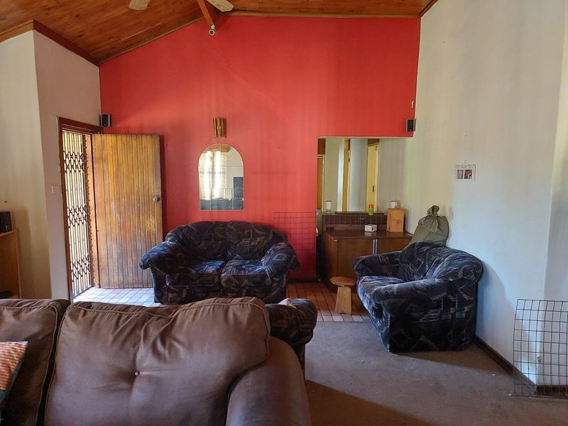 Living room featuring a vaulted timber ceiling, security gate access, and a built-in vanity or bar area with dated finishes.