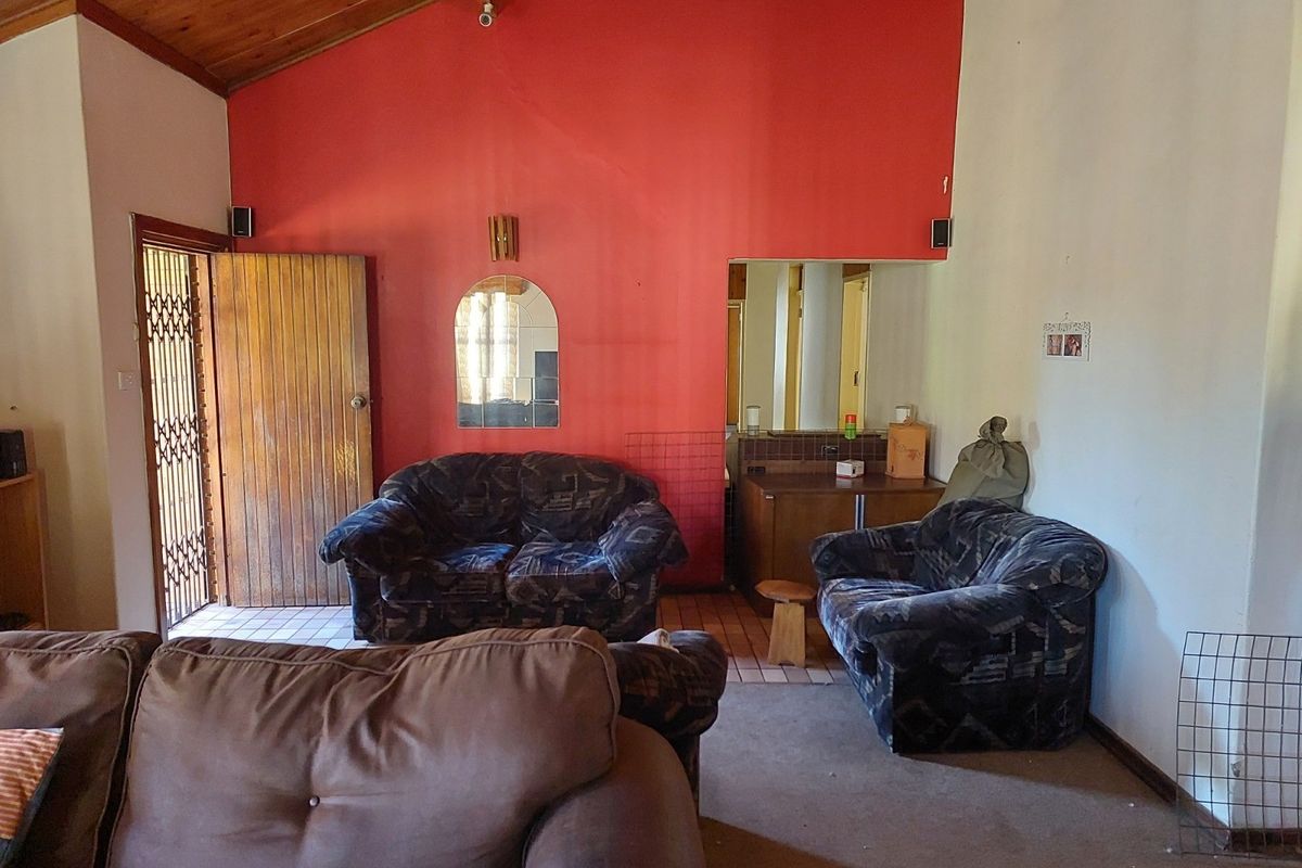 Living room featuring a vaulted timber ceiling, security gate access, and a built-in vanity or bar area with dated finishes.