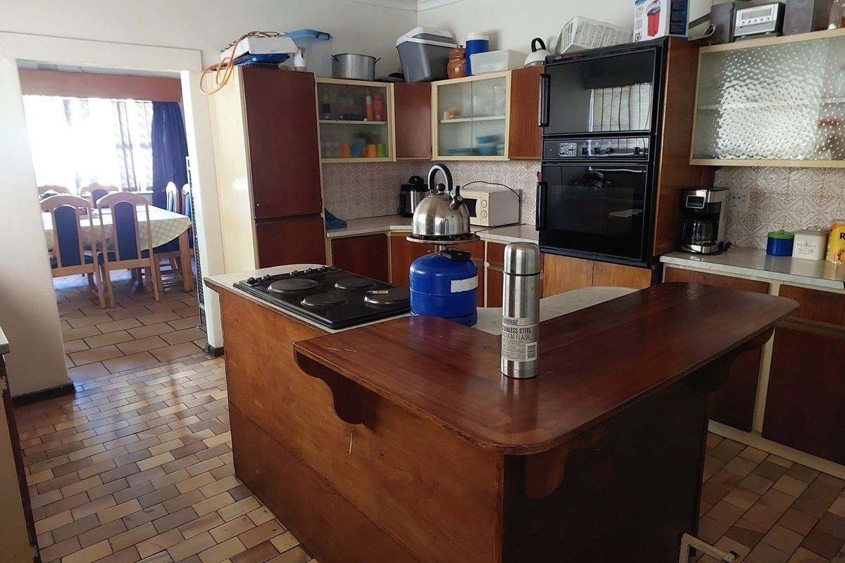 A dated kitchen featuring wooden cabinetry, a built-in double oven, electric hob, and tiled flooring, offering significant potential for a modern renovation.