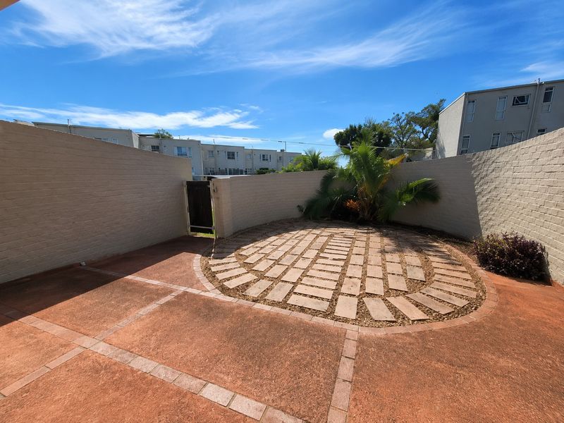 A private, paved outdoor patio area enclosed by brick boundary walls, featuring a circular paved design and a pedestrian access gate.