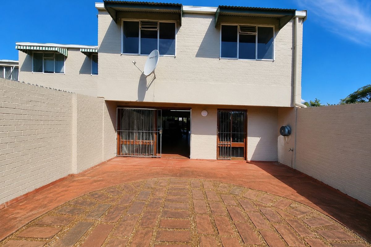 Rear exterior view of the property featuring a paved courtyard, security gates, and brick facade with upper-level windows.