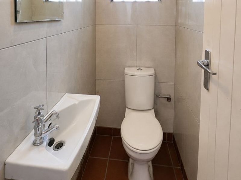 A compact guest bathroom featuring a wall-mounted basin, toilet, tiled finishes, and a glass block window for natural light.