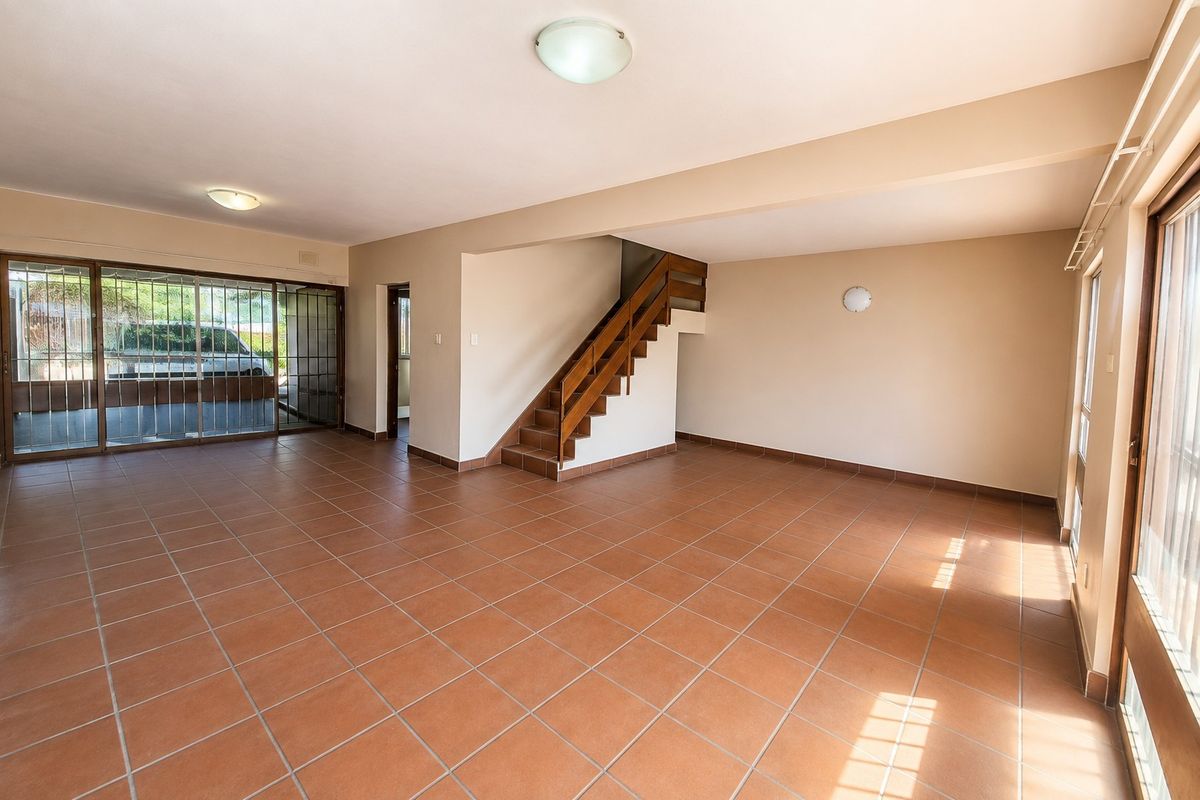Spacious open-plan living area featuring terracotta floor tiles, a wooden staircase, and large sliding glass doors providing natural light.
