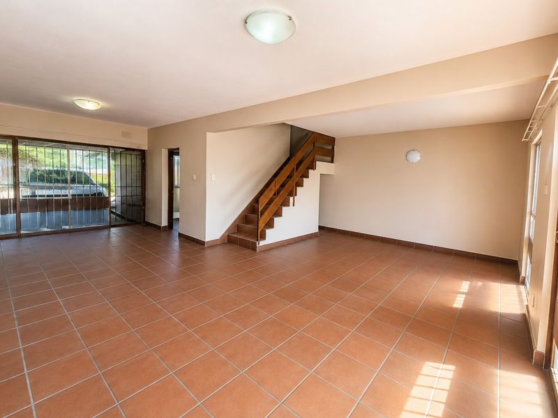 Spacious open-plan living area featuring terracotta floor tiles, a wooden staircase, and large sliding glass doors providing natural light.