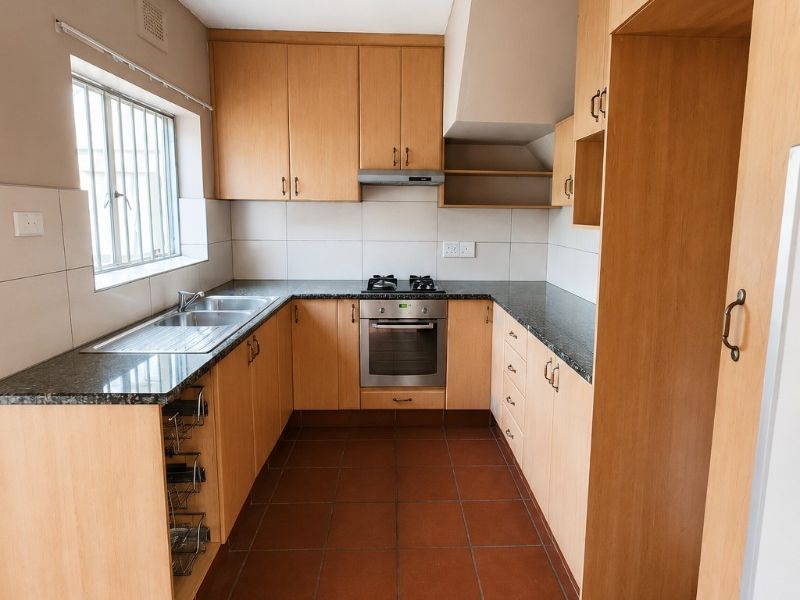 A functional kitchen featuring light wood cabinetry, granite countertops, built-in oven with gas hob, and durable tiled flooring.