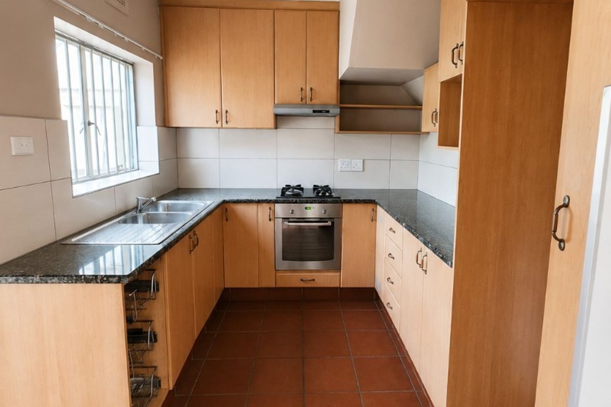 A functional kitchen featuring light wood cabinetry, granite countertops, built-in oven with gas hob, and durable tiled flooring.