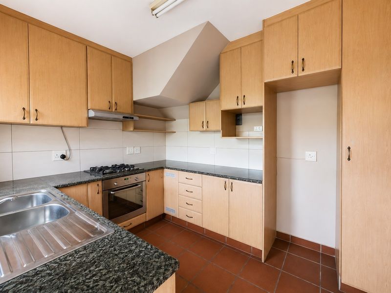 A functional kitchen featuring light wood cabinetry, granite countertops, a built-in oven with gas hob, and tiled flooring.