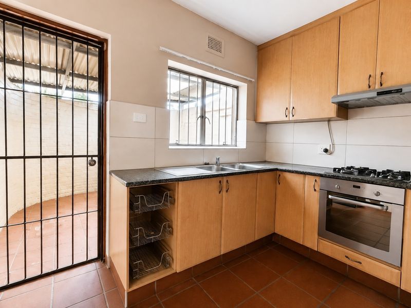 Functional kitchen featuring light wood cabinetry, granite countertops, built-in oven with gas hob, and direct access to an outdoor area through a security gate.