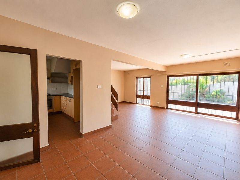 Spacious open-plan living area featuring tiled floors, large sliding glass doors with security gates, and an adjacent kitchen with built-in cabinetry.