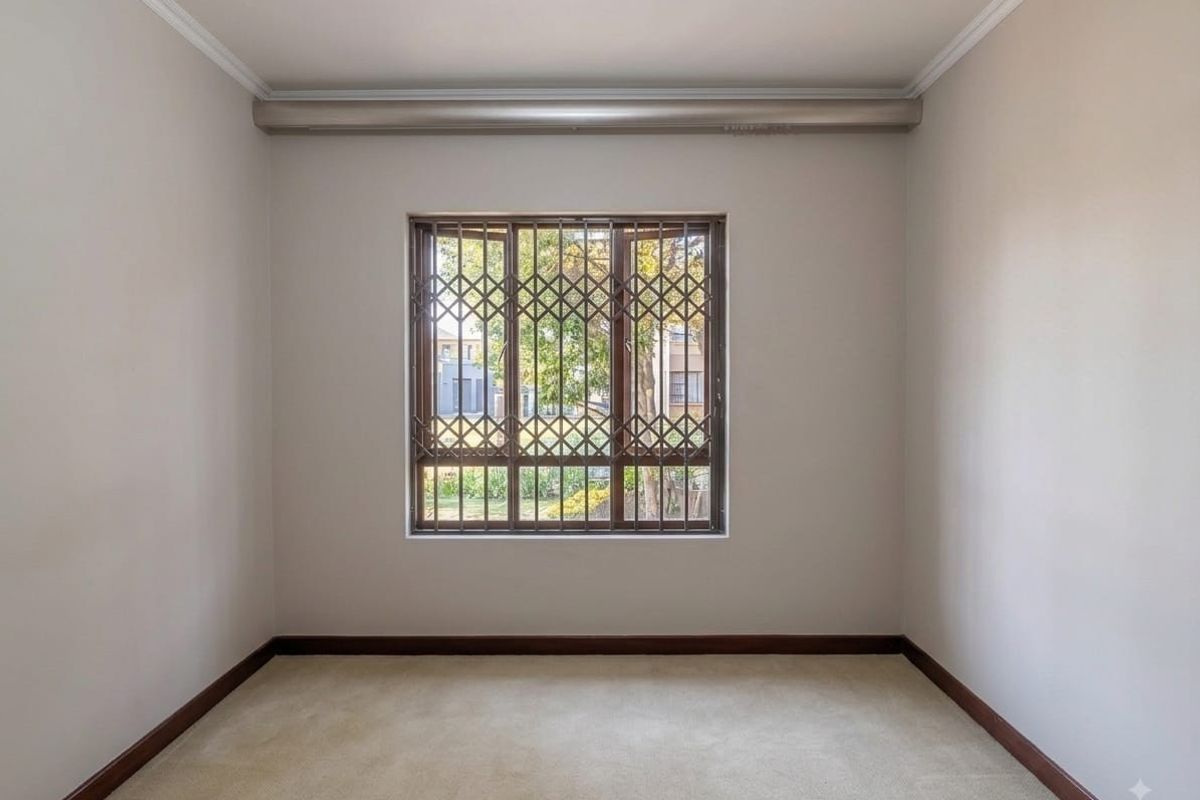 An empty bedroom featuring neutral walls, carpet flooring, and a window fitted with a security gate.