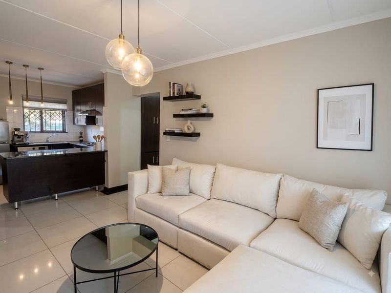 Modern open-plan living area featuring a sleek kitchen with dark cabinetry, granite countertops, and tiled flooring, seamlessly flowing into the comfortable lounge space.
