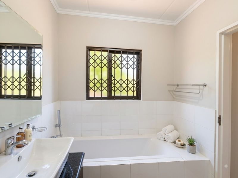 A clean and well-maintained bathroom featuring a built-in bathtub, vanity basin with chrome fixtures, and a window with security bars.