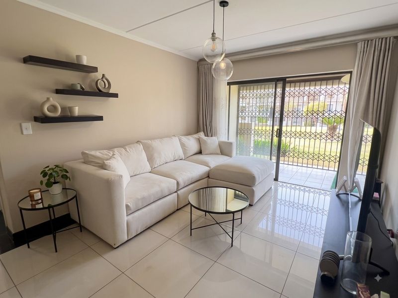 A bright and modern living room featuring large format floor tiles, contemporary pendant lighting, and a sliding door leading to an outdoor patio area.