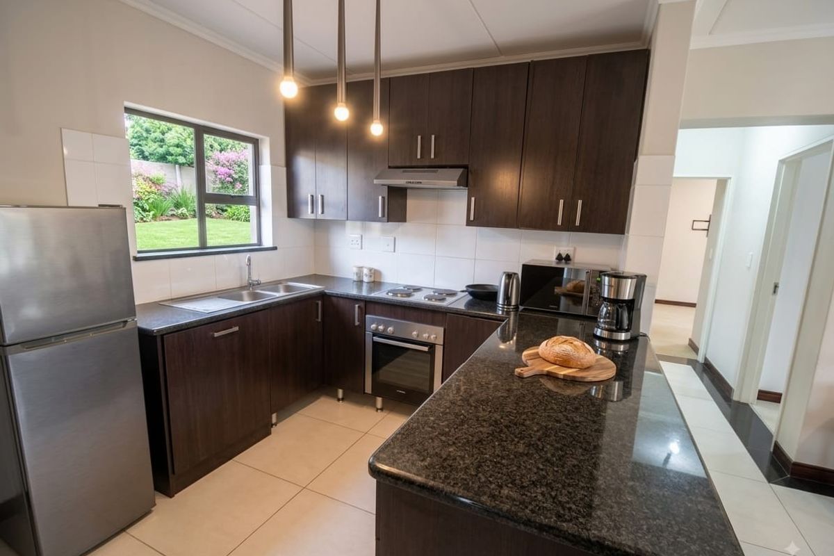 Modern kitchen featuring dark wood cabinetry, granite countertops, built-in oven, hob, and extractor fan, with tiled flooring and a view of the garden.