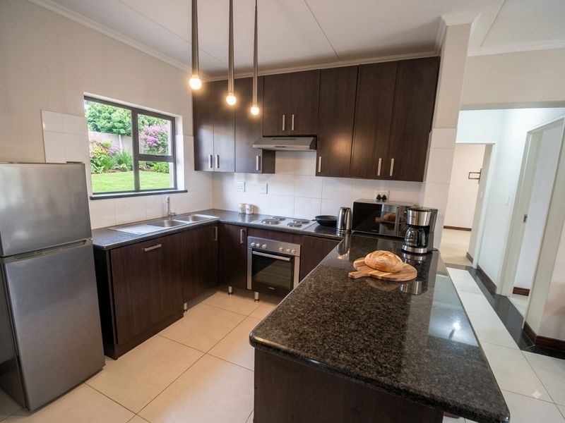 Modern kitchen featuring dark wood cabinetry, granite countertops, built-in oven, hob, and extractor fan, with tiled flooring and a view of the garden.