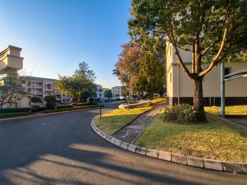 A well-maintained apartment complex exterior featuring paved driveways, manicured lawns, and established trees within a residential estate setting.