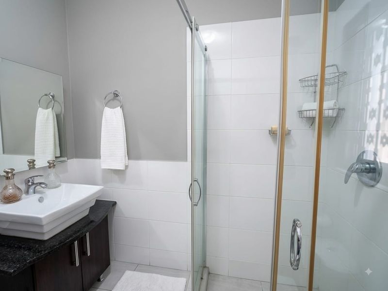 Modern bathroom featuring a dark wood vanity with granite countertop, vessel sink, and a glass-enclosed shower with white wall tiling.