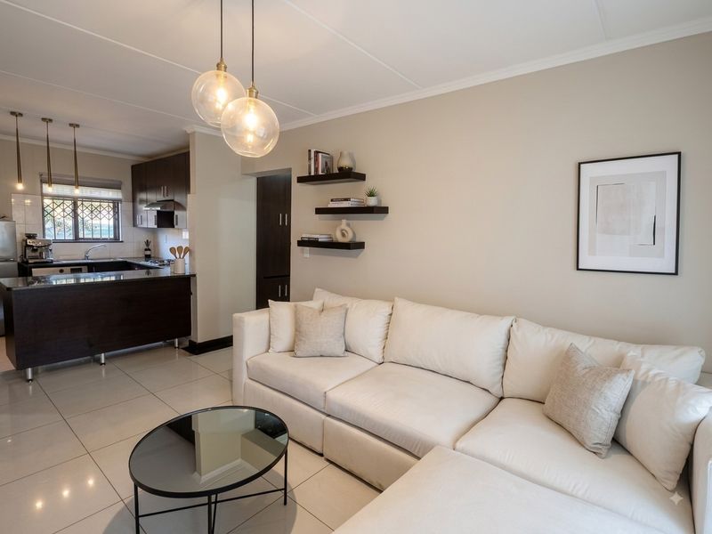 Modern open-plan living area featuring a sleek kitchen with dark cabinetry, granite countertops, and tiled flooring, seamlessly flowing into the comfortable lounge space.