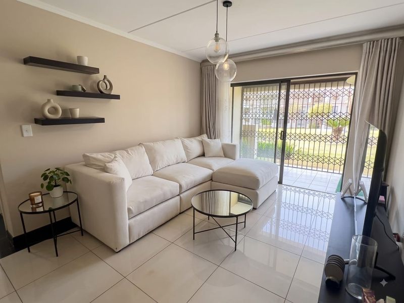 A bright and modern living room featuring large format floor tiles, contemporary pendant lighting, and a sliding door leading to an outdoor patio area.