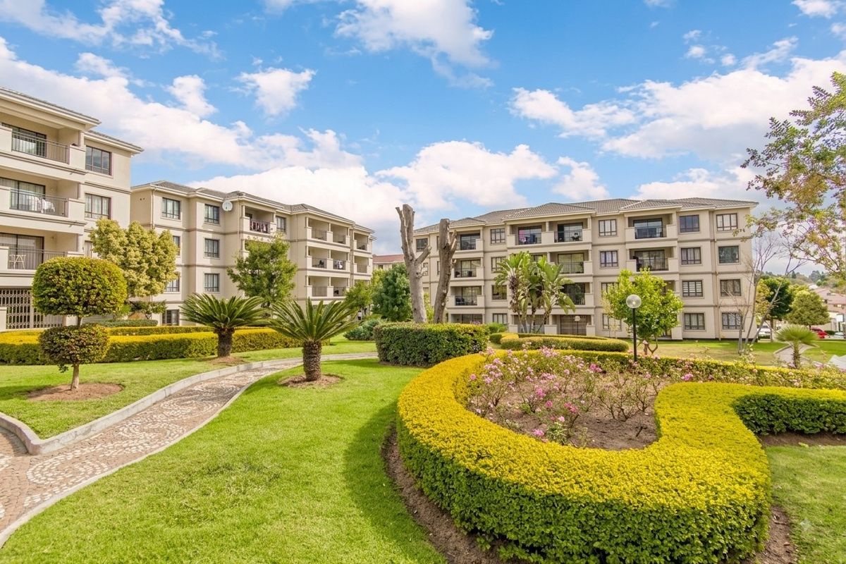 Well-maintained communal garden area featuring manicured hedges, lawns, and paved pathways set against the backdrop of a multi-story apartment complex.