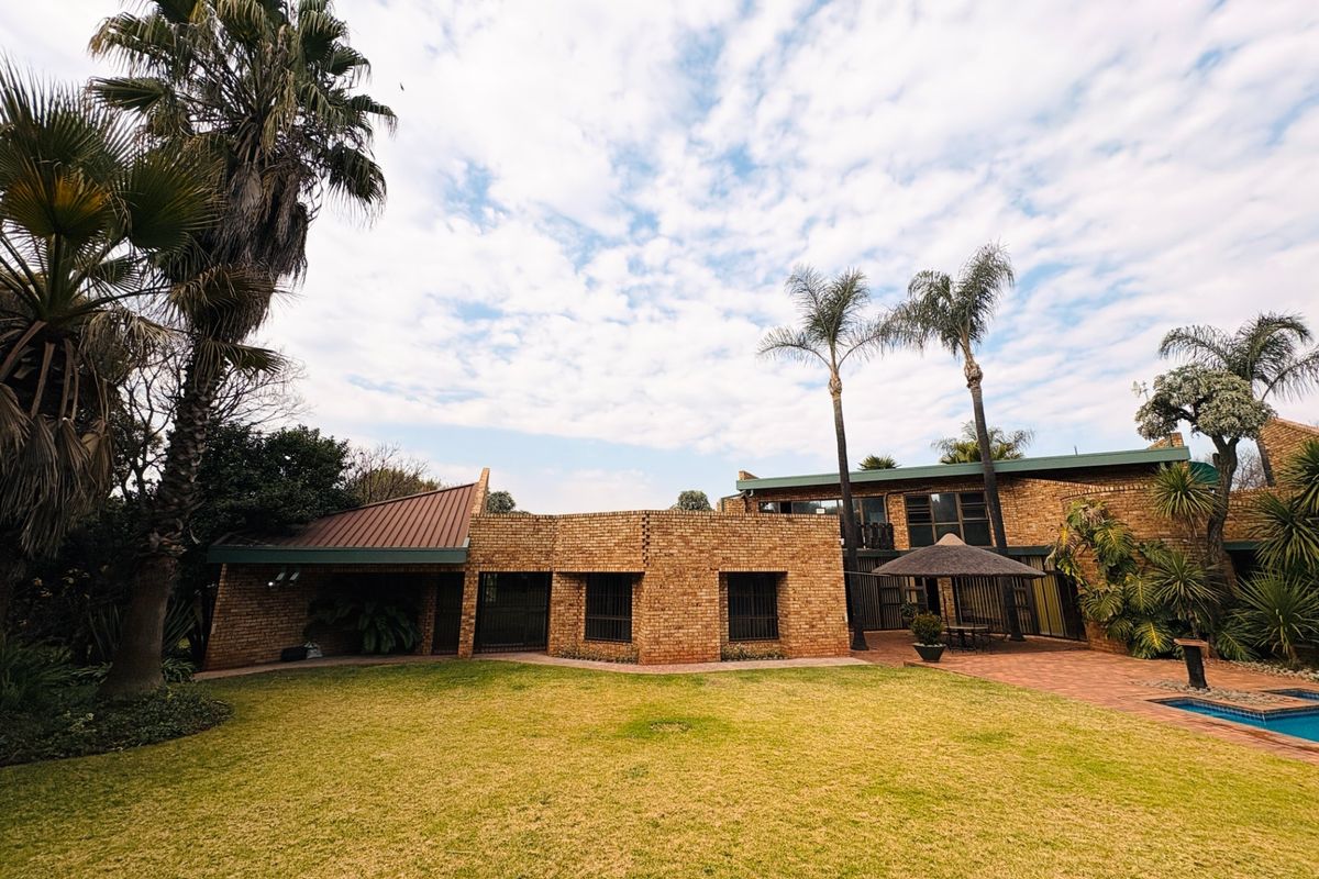 Rear view of a face brick house featuring a spacious lawn, paved patio area, and a swimming pool.