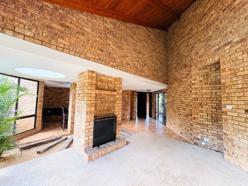 Spacious living area featuring high vaulted timber ceilings, exposed brick walls, a built-in fireplace, and large windows providing ample natural light.