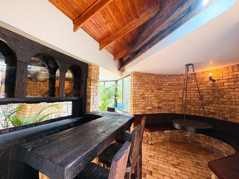 A rustic bar area featuring exposed timber beams, brick walls, built-in brick bench seating, and a unique hanging fireplace.
