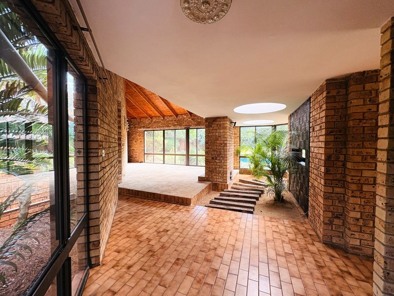 Spacious living area featuring exposed brick walls, tiled flooring, a timber vaulted ceiling, and unique internal garden features with natural light from skylights.