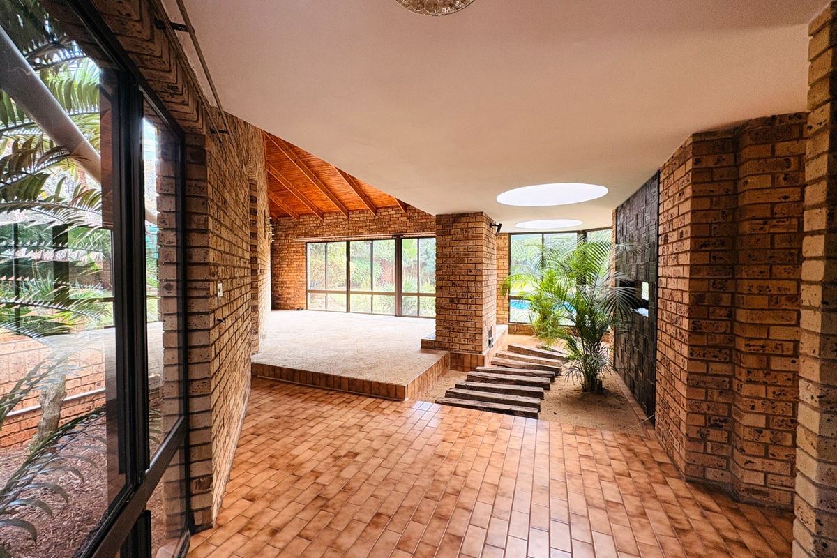 Spacious living area featuring exposed brick walls, tiled flooring, a timber vaulted ceiling, and unique internal garden features with natural light from skylights.