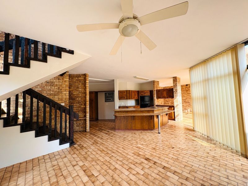 Spacious open-plan living and kitchen area featuring exposed brick walls, tiled flooring, and a central staircase, offering a blank canvas for modern renovation.