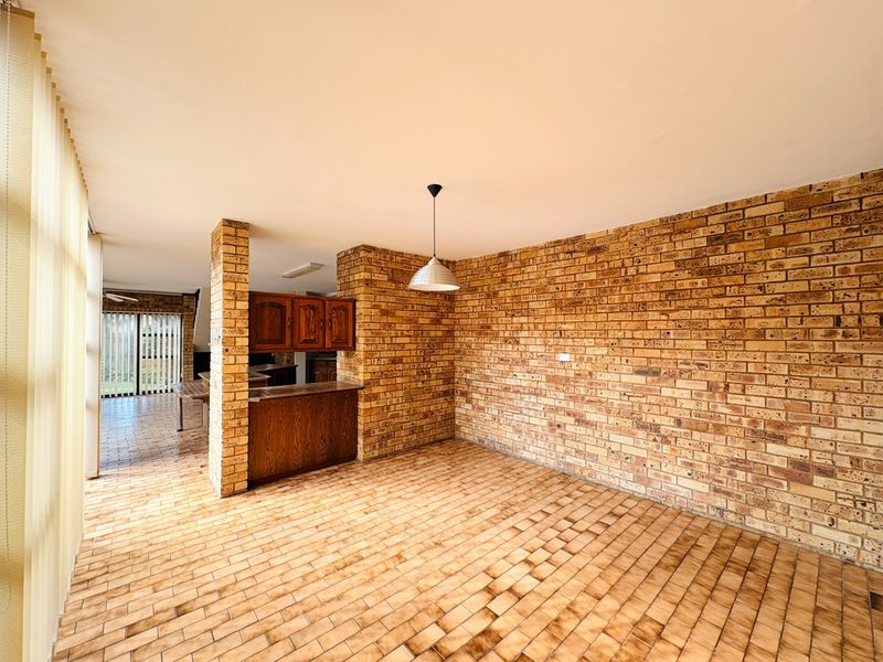 Spacious open-plan living area featuring exposed brick walls, tiled flooring, and built-in wooden cabinetry, offering a versatile layout with abundant natural light.