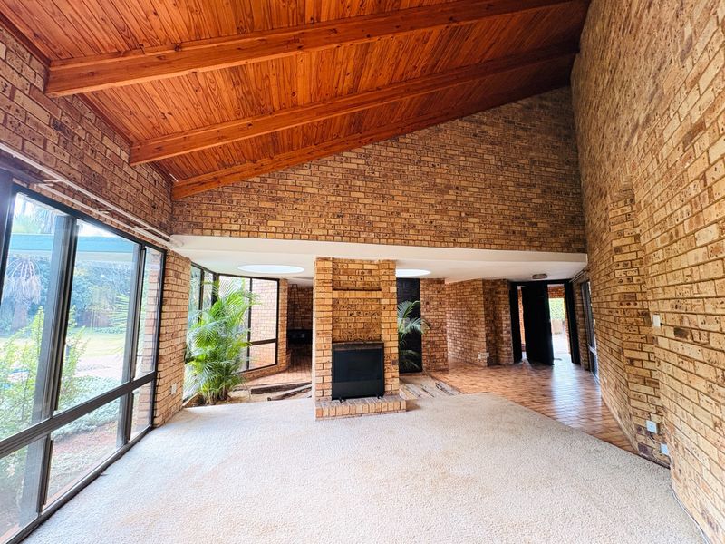Spacious living area featuring a dramatic raked timber ceiling, exposed face brick walls, a central built-in fireplace, and large windows overlooking the garden.