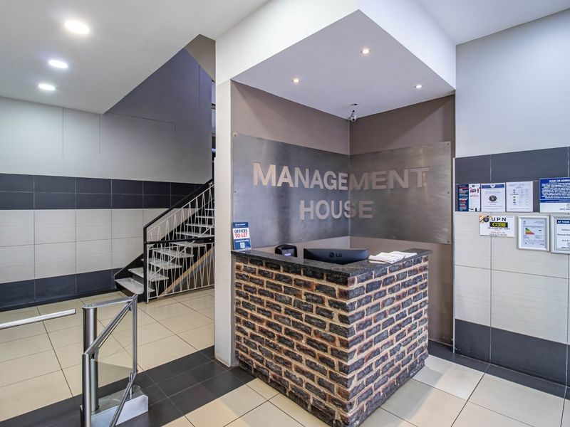 Commercial building entrance featuring a brick-faced reception desk, metal signage, secure turnstile access, and a staircase leading to upper levels.