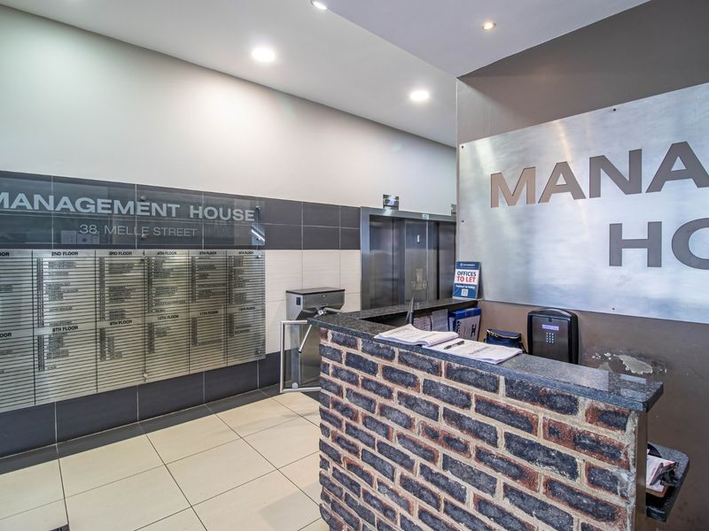 Commercial building entrance lobby featuring a brick-faced reception desk, directory signage, elevator access, and secure turnstile entry.