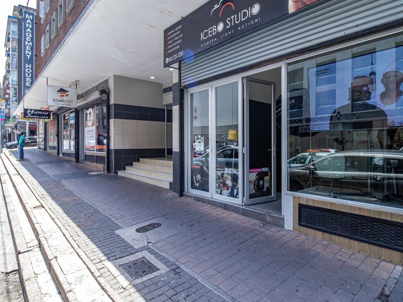 Street-level view of a commercial storefront featuring a glass entrance, paved sidewalk access, and prominent signage in an urban setting.
