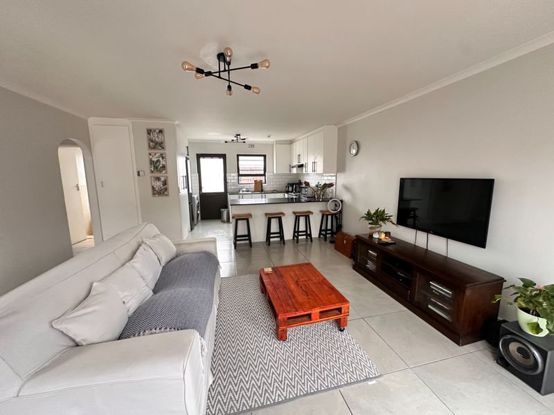 An open-plan living and kitchen area featuring tiled flooring, modern cabinetry, a breakfast bar, and a subway tile backsplash.
