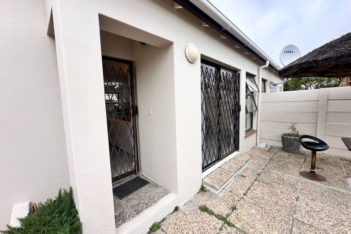 Rear exterior view featuring a paved patio area, security gates on sliding doors, and a boundary wall.