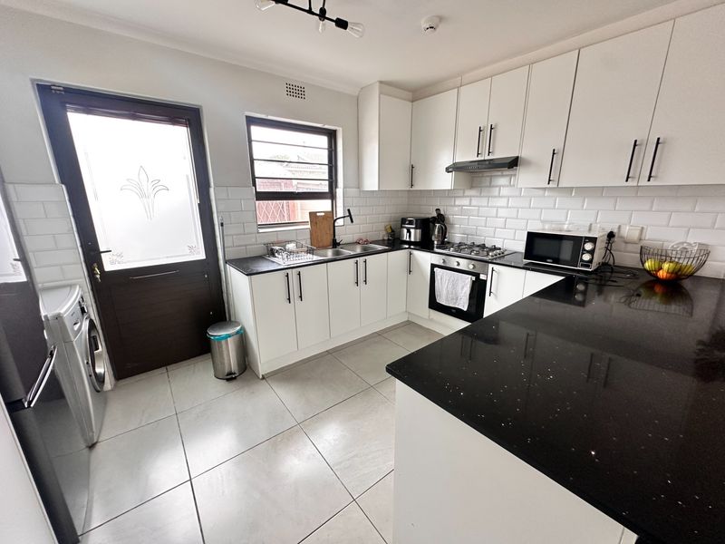 Modern kitchen featuring white cabinetry, contrasting black granite countertops, subway tile backsplash, built-in gas hob, oven, and direct access to the exterior.