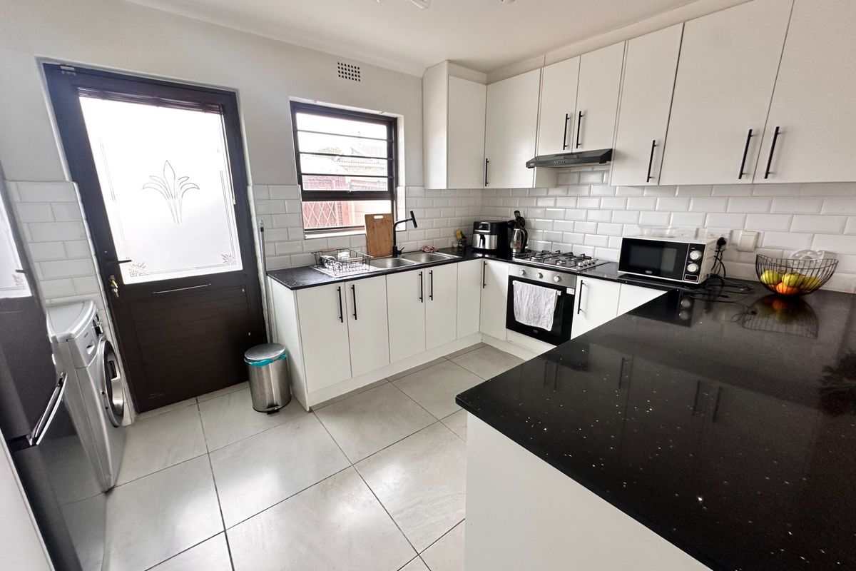 Modern kitchen featuring white cabinetry, contrasting black granite countertops, subway tile backsplash, built-in gas hob, oven, and direct access to the exterior.