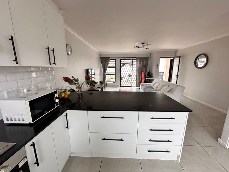 Modern open-plan living area featuring a contemporary kitchen with white cabinetry, black stone countertops, subway tile backsplash, and seamless flow to the lounge area.