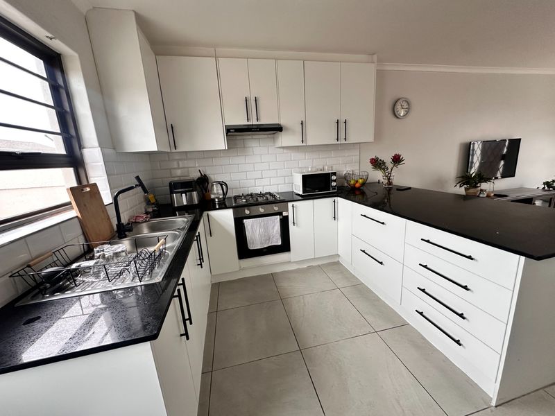 Modern kitchen featuring white cabinetry, contrasting black granite countertops, subway tile backsplash, and integrated gas hob with oven.