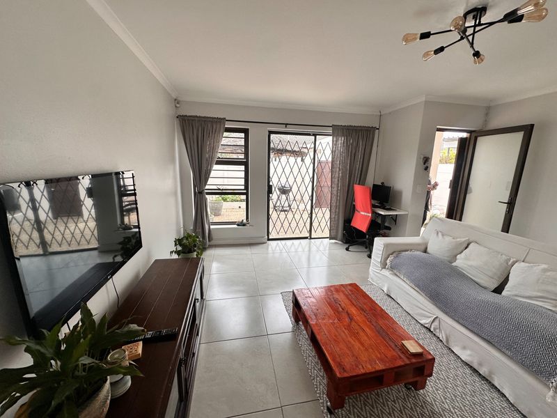 A bright and well-maintained living room featuring tiled flooring, modern lighting, and a sliding glass door providing access to the outdoor area.